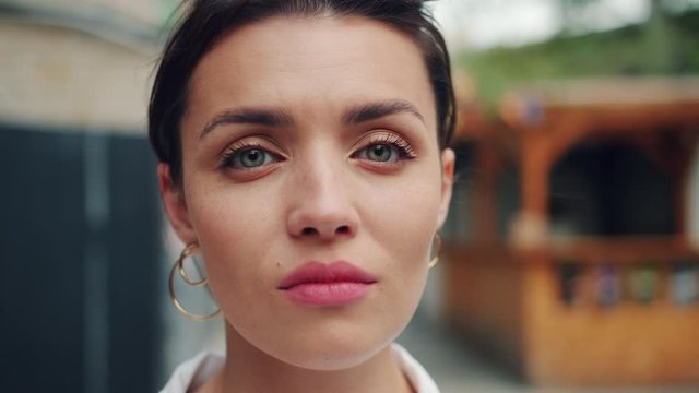 Slow Motion Portrait Of Young Adult Woman With Serious Face Standing Outdoors And Looking At Camera. Attractive People, Modern City And Emotions Concept.