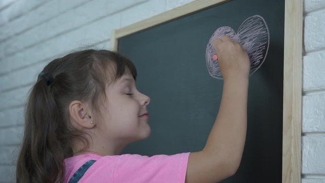 A heart from chalk. Cute little girl draws a heart with chalk on a school board.