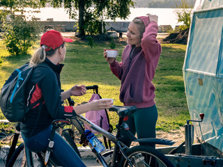 Two young girls in sportswear are resting after a bike ride. They drink tea, laugh and talk.