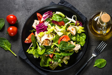 Green salad with chicken and vegetables on black.