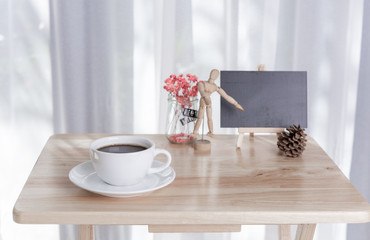 Blank black board with coffee cup and dried flower on office table with white curtain background