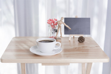 Fototapeta na wymiar Blank black board with coffee cup and dried flower on office table with white curtain background