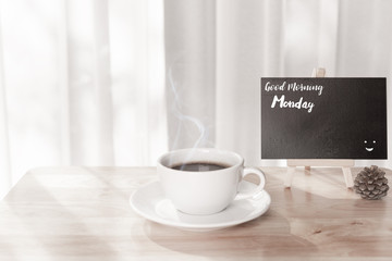 Good morning Monday text on black board with coffee cup on office table with white curtain background