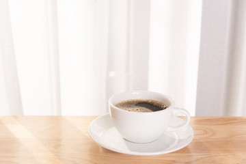 White coffee cup  on wooden office desk  with morning sunlight and  soft curtain background