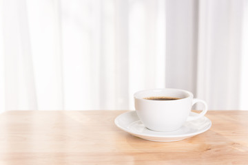 White coffee cup  on wooden office desk  with morning sunlight and  soft curtain background