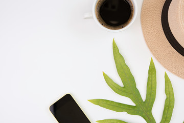 Workspace compositon with mobile phone,coffee cup, green leaves and panama hat with space on white background,top view