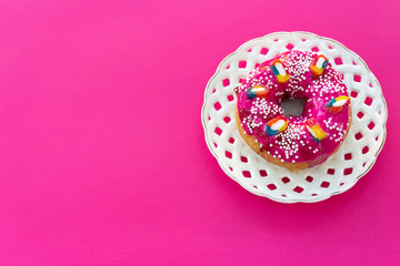 Obraz na płótnie Canvas Donut with bright sugar pink icing on a white openwork plate on a pink purple table background with place for text for design.