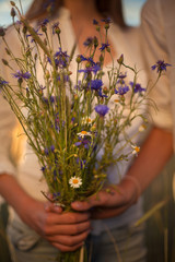A happy young girl in a white shirt is holding a bouquet of wild flowers in her hands, which the boy gave her. Photo without face. Romantic relationship between two young people. love story concept.