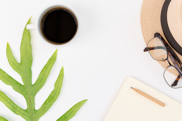 Office workspace with notebook,coffee,eyeglass,green leaf and panama hat on white background,top view