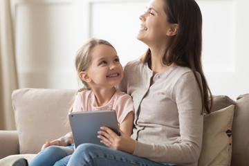 Laughing mother and little daughter watching cartoons on tablet