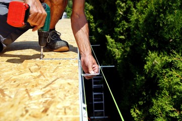 preparation of iron brackets of a roof gutter which are screwed on construction site.male Hand of...