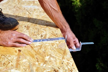 preparation of iron brackets of a roof gutter which are screwed on construction site.male Hand of carpenter holds a tool.gutters water drainage system.roofer installs roof gutter system. spirit level.