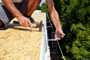 preparation of iron brackets of a roof gutter which are screwed on construction site.male Hand of carpenter holds a tool.gutters water drainage system.roofer installs roof gutter system. spirit level.