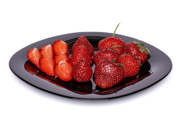 Whole and sliced strawberries on a black plate