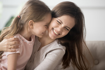 Laughing mother playing with daughter embrace her having fun together