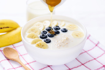Pouring honey on oatmeal with banana and blueberry in a bowl, healthy breakfast
