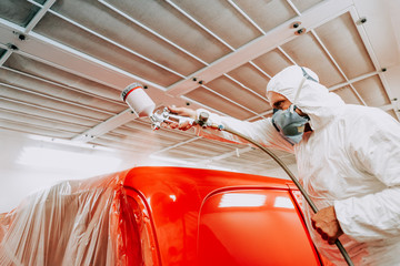 Automotive mechanical engineer painting the body of a red car with special suit.