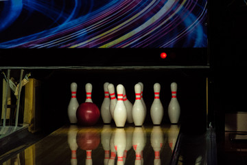 Rolling red ball knocks down pins on a bowling alley lane