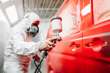 Close-up of worker using spray gun and airbrush and painting a red car