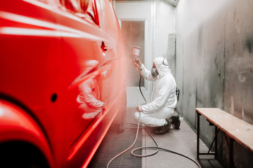 Automotive industry manufacturing details - painter working on applying red paint on a van