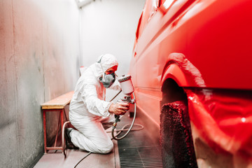 Mechanic working on painting a red car in special booth