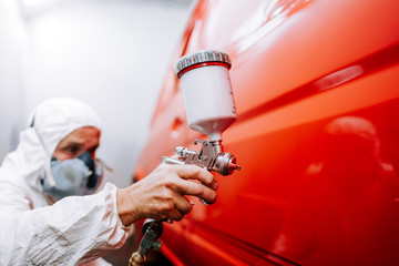 mechanic worker painting a car in a special painting box, wearing a full body costume and...