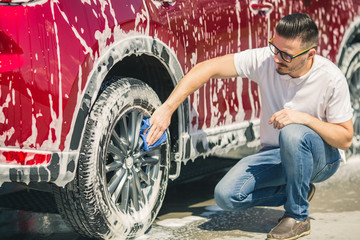 Plakat Car detailing - the man holds the microfiber in hand and polishes the car. Selective focus. Car detailing series : Worker cleaning red car. 