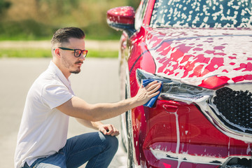 Car detailing - the man holds the microfiber in hand and polishes the car. Selective focus. Car detailing series : Worker cleaning red car. 