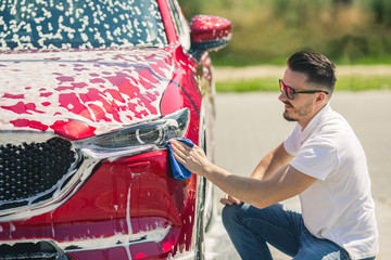 Car detailing - the man holds the microfiber in hand and polishes the car. Selective focus. Car detailing series : Worker cleaning red car. 