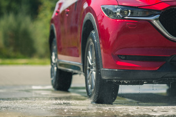 Fototapeta premium Red car with white soap on the body in car care shop. Isolated on background. Manual car wash with pressurized water in car wash outside.
