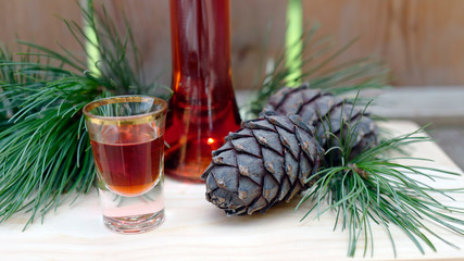 a glass liquor, cones and twigs from the swiss stone pine or arolla on a wood board