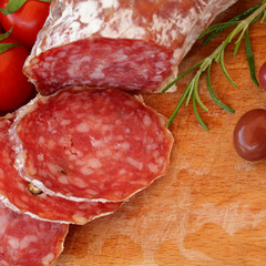 Gourmet food - salami, olives and rosemary herbs on wooden table