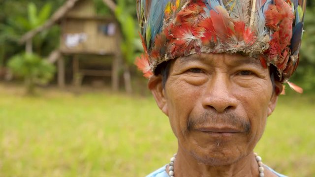 Portrait Of An Old, Indigenous, Amazonian Man Standing In His Village Wearing Traditional Outfit And A Colorful Hat Slow- Motion, Close Up Shot