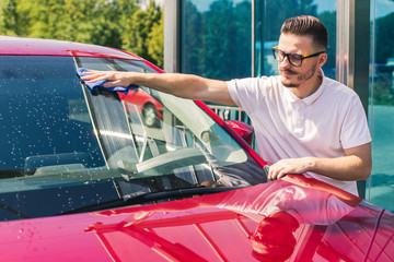 Car detailing - the man holds the microfiber in hand and polishes the car. Selective focus. Car detailing series : Worker cleaning red car. 