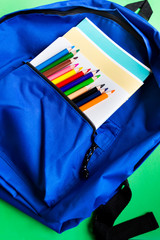 School backpack with notebooks and pencils on a paper green background. Flat lay