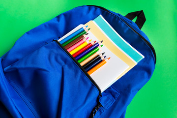 Notebooks and multi-colored pencils in a backpack on a paper green background. School accessories. Top view
