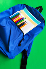 Notebooks and multicolored pencils in a backpack on a paper green background. School accessories. Top view