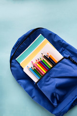 School backpack with notebooks and pencils on a paper blue background with copy space. School Supplies. Top view