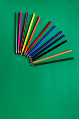 Set of multicolored wooden pencils on a green paper background with copy space. School accessory. Flat lay