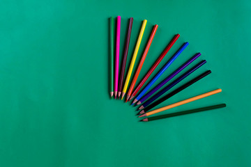Collection of multicolored wooden pencils on a dark green paper background with copy space. School supplies. Flat lay