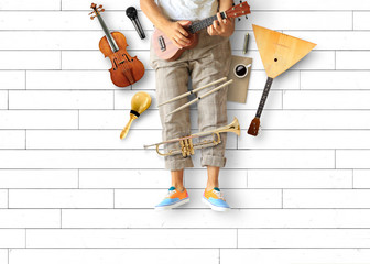 Young man sits and playing guitar among musical instruments