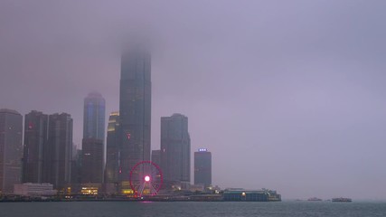 Time lapse day to night of Hong Kong cityscape with hard mist at the harbor in the raining day