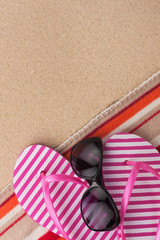 Summer accessories flip flops and towel. Sand beach texture background.