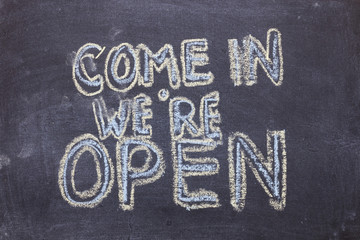 Come in we're open. Chalk lettering on blackboard. Multi colored inscription