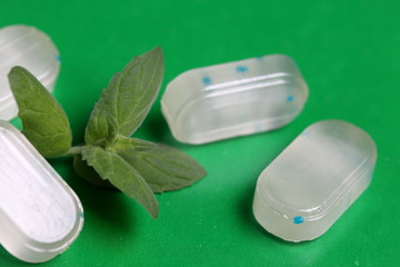Peppermint candies for breath freshening. With refreshing microgranules. Cooling menthol for sore throat. Nearby are fresh mint leaves. On a green background.