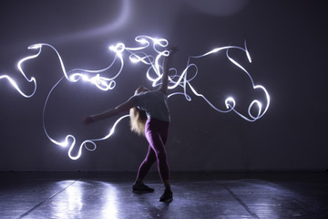 Modern art dancer, dancing in front of a black background with neon blue light while stretching and twisting her body., long exposure blur
