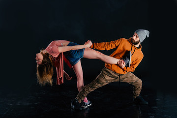 Couple dancing modern dance and showing off their leg stretch moves.Black background while the couple is dressed in urban colorful clothes...