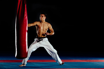 Boxer agressively punching with a kick a sand bag isolated on black wall