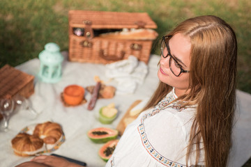 Happy blonde young girl with glasses enjoying a picnic on the outdoors, on the grass