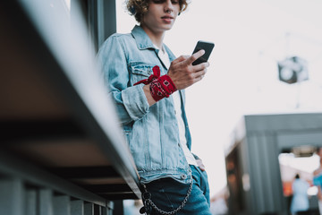 Calm man in jeans coat standing with smartphone